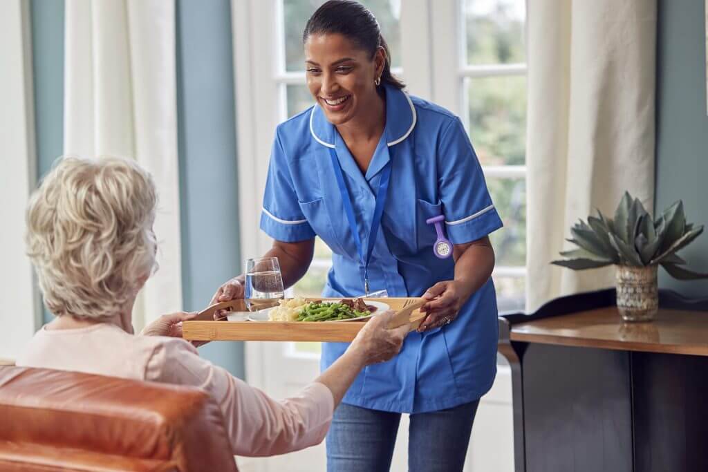 female care worker in uniform bringing meal on tra